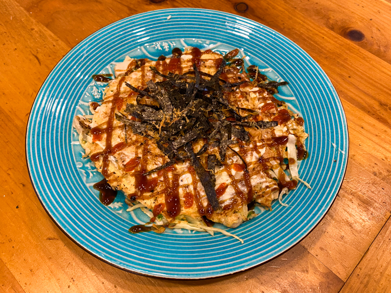 A pancake topped with sauce and seaweed on a plate